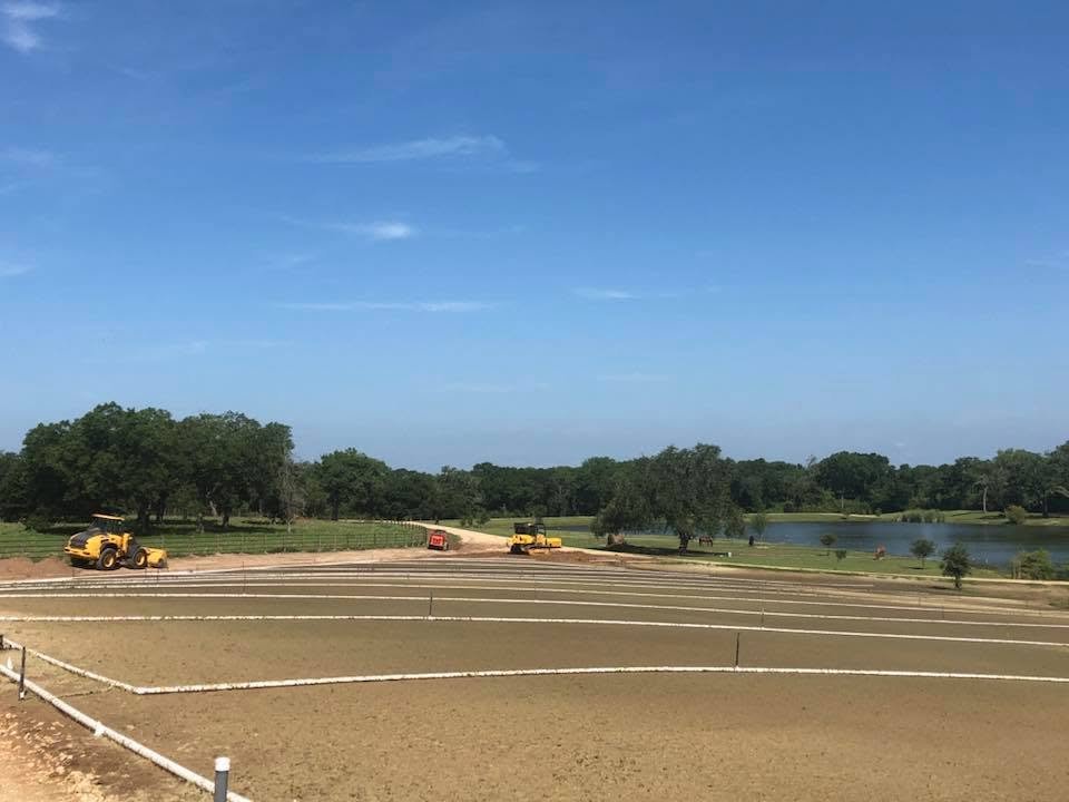 Pastures being regraded beside a pond, with a loader and track loader working in the distance