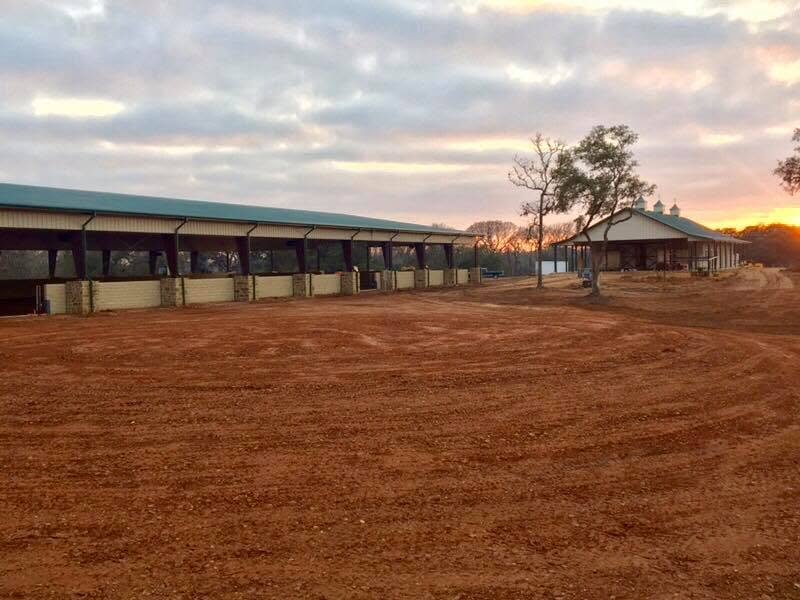 Regraded red dirt in front of the stone-walled covered arena at sunset