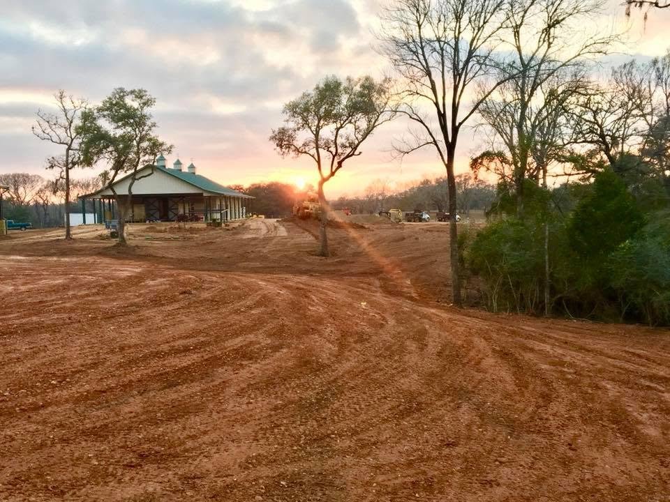 Rough grade at sunrise, the barn and oaks beyond freshly cut red dirt