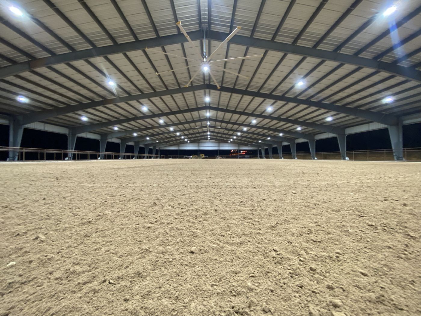 Ground-level view of finished, groomed footing across a covered arena at night