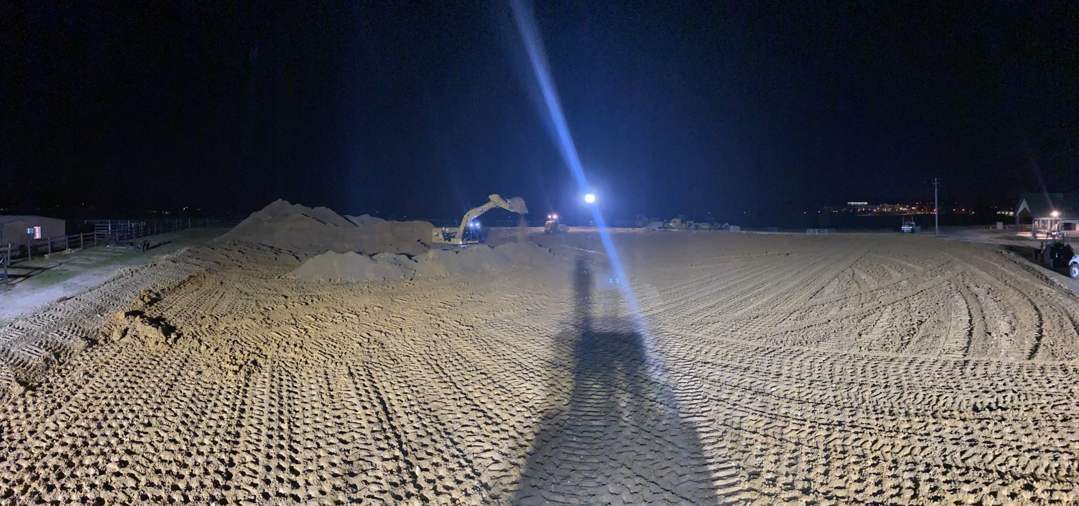 A freshly laser-graded arena pad at night, lit by a single work light