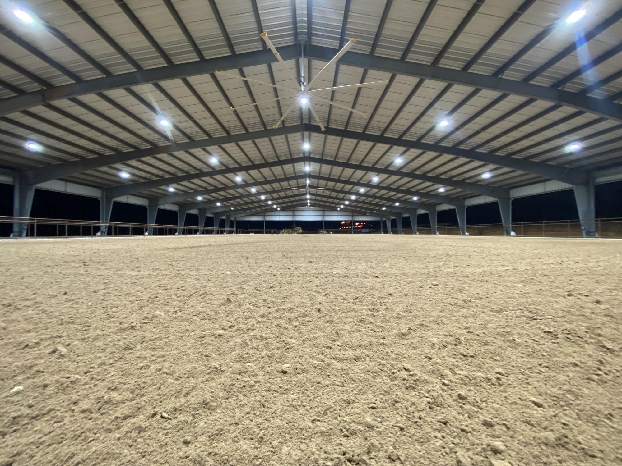 A finished covered arena at night, its footing groomed dead level under rows of LED lights