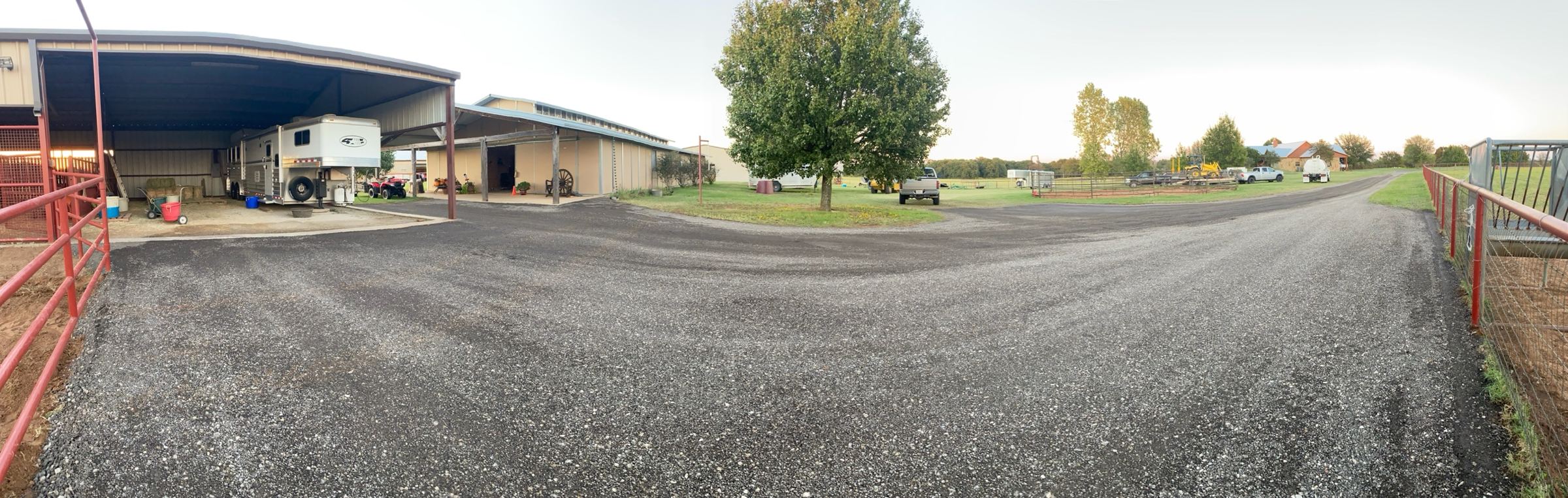 Panorama of a finished horse property: gravel drive sweeping past the barn, covered trailer parking and pens