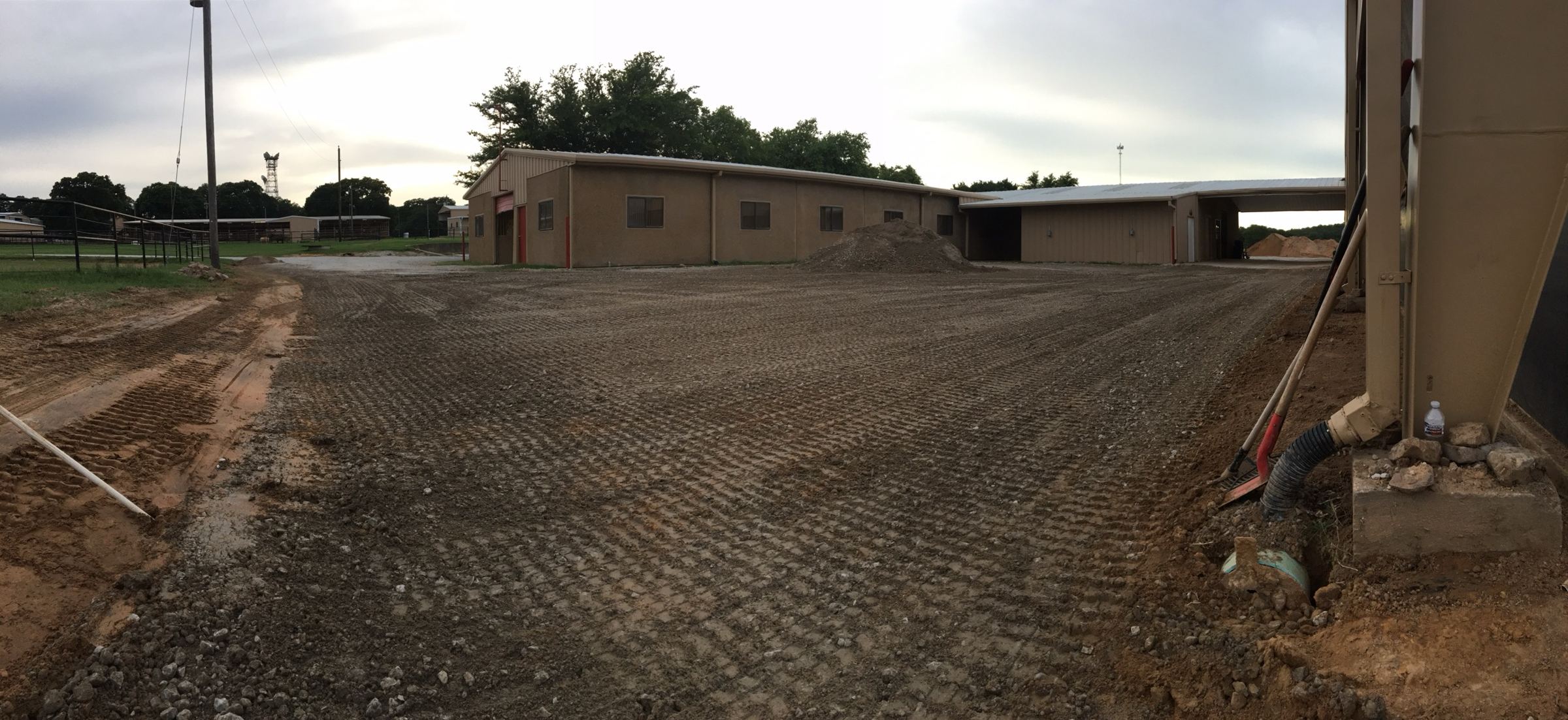 Freshly graded pad around a barn, sloped away from the building with the downspout piped underground